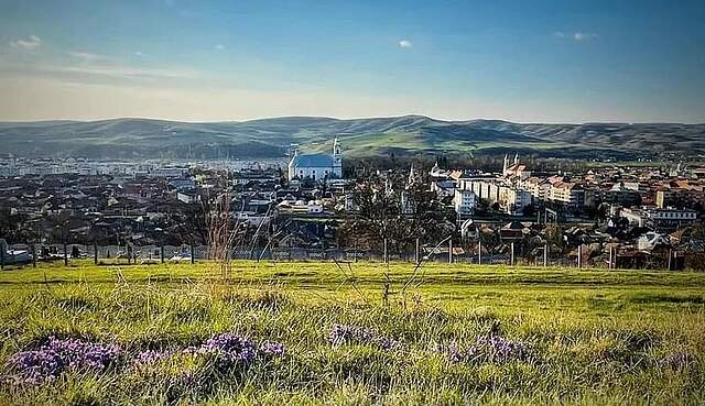 Die Partnerstadt Gherla umgeben von einer idyllischen Landschaft. Eine Stadt liegt vor einer hügeligen Landschaft. Im Vordergrund befindet sich eine große Wiese.