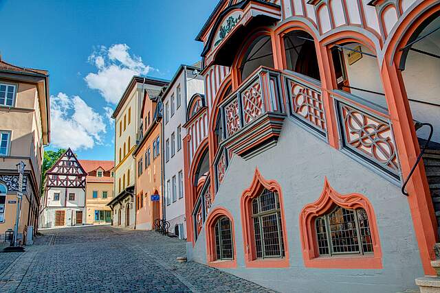 Historische und aufwändig verzeirte Rathaustreppe in Pößneck mit bunten Häusern in der Nachbarschaft in der Altstadt.