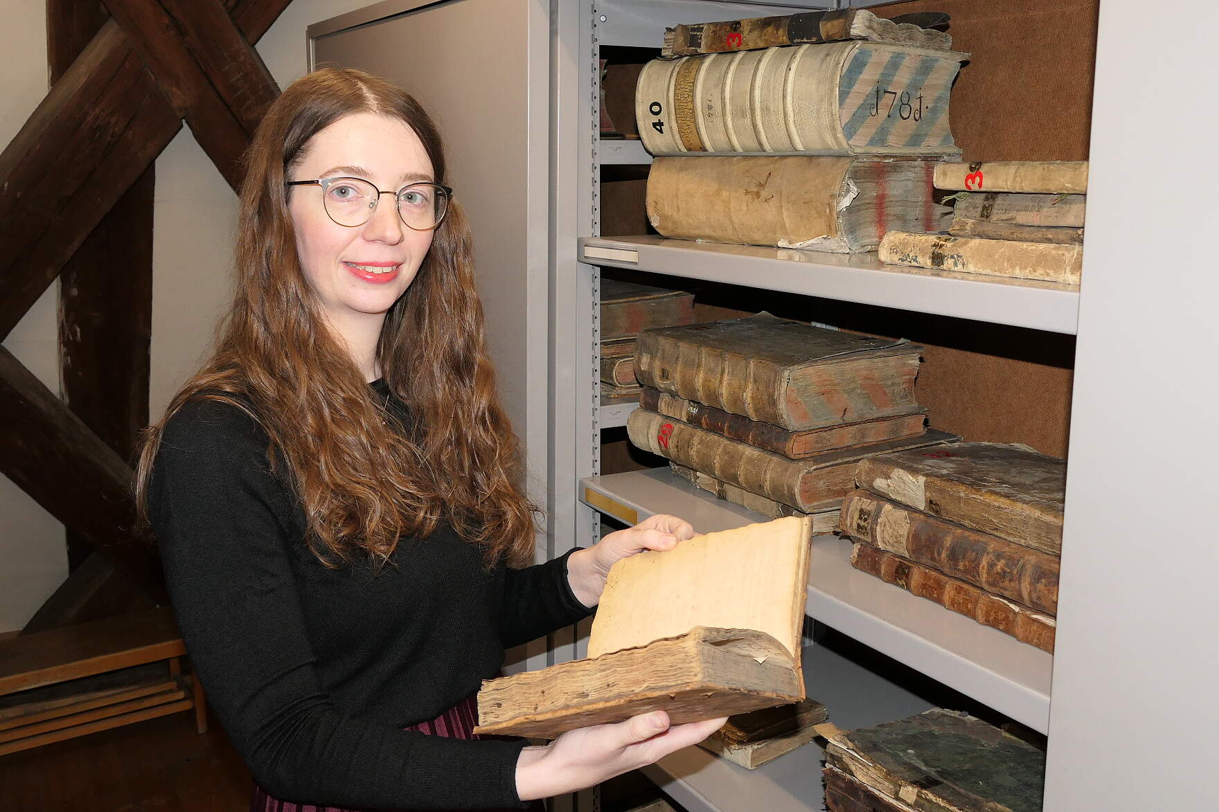 Stadtarchivarin Miriam Mulzer mit einem aufgeschlagenem Buch vor einem Regal im Stadtarchiv