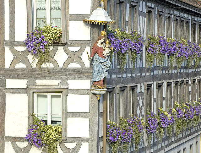 Außenansicht eines Fachwerkgebäudes mit Blumenschmuck und einer Marienfigur am Gebäudeeck.