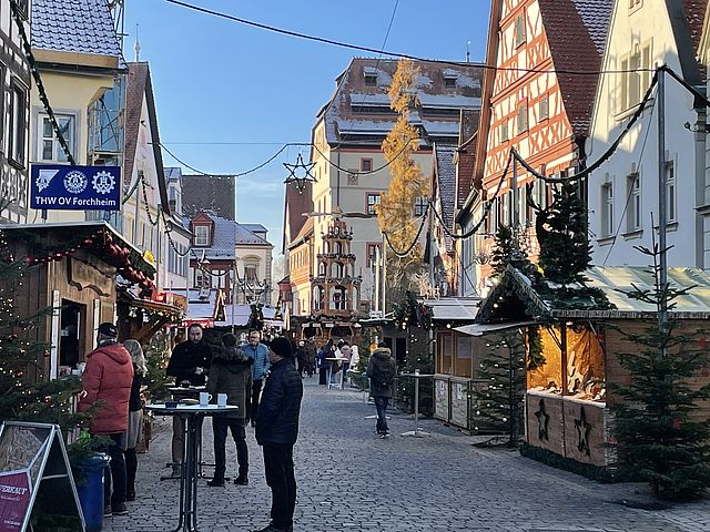 Ein Weinnachtsmarkt mit geschmückten Buden und weihnachtlicher Beleuchtung umrahmt von Stadthäusern und den mächtigen Bau der Kaiserpfalz Forchheim..