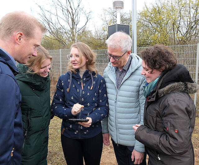 Personen um ein Tablet bei der Einweihung der Wetterstationen