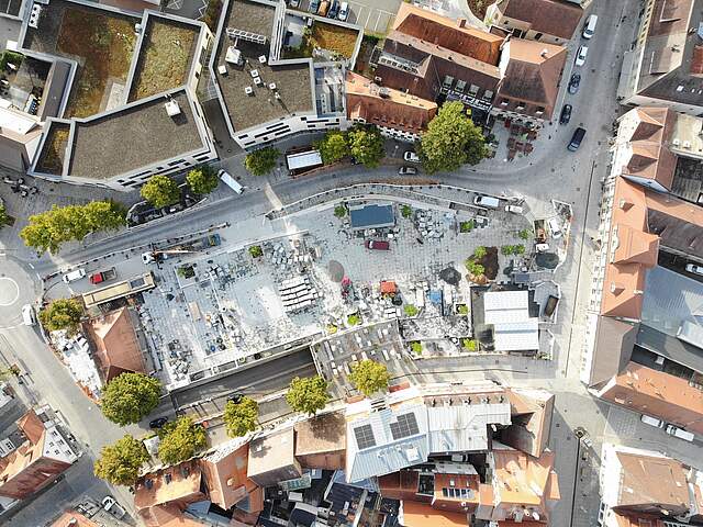 Eine Luftbildaufnahme zeigt die Umbaumaßnahmen auf einem großen Stadtplatz mit Pflasterarbeiten, Baumaterial und neuen Bäumen.