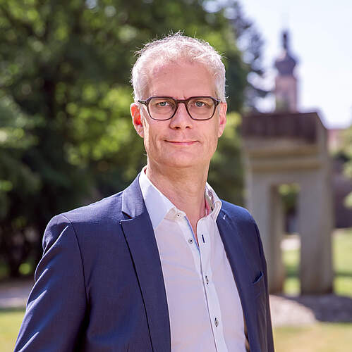 Oberbürgermeister Dr. Uwe Kirschstein im Forchheimer Stadtpark. Im Hintergrund ein Denkmal und die Martinskirchturmspitze.