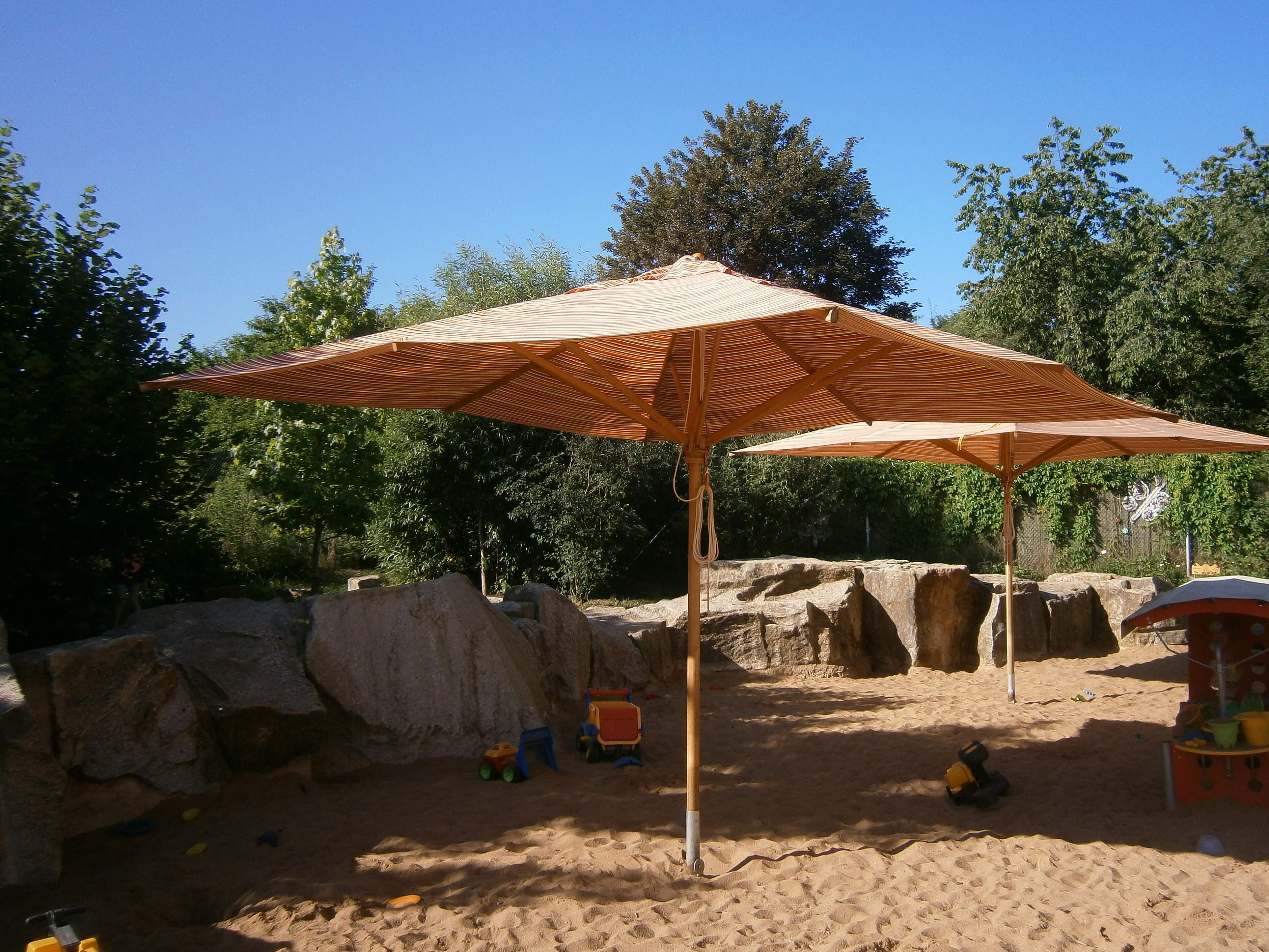 Der Außenbereich einer städtischen Kita mit Sandkasten und Sonnenschirm