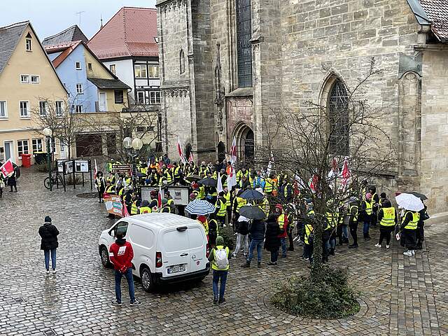 Eine große Gruppe streikender Mitarbeiter auf einem Platz vor einer Kirche