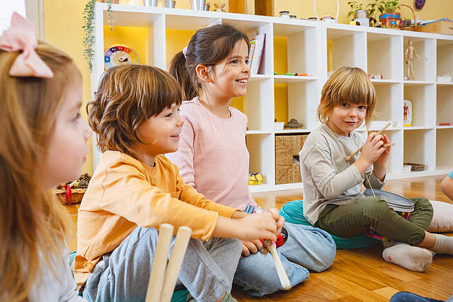 Kindergartenkinder Kindergartenkinder im Morgenkreis in einen Gruppenraum. Im Hintergrund steht ein offenes weißes Regal mit Spielsachen.