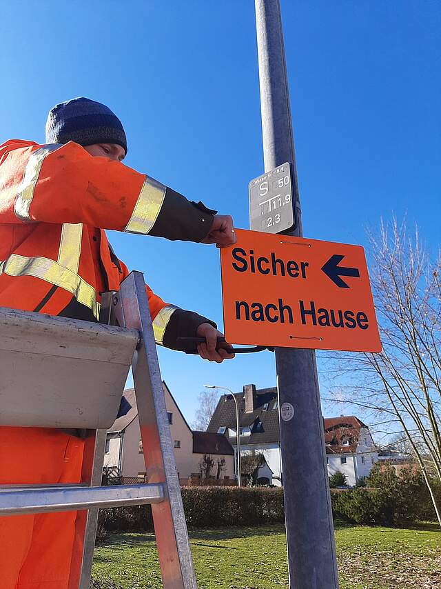 Mann hängt Schild mit Text "Sicher nach Hause" auf