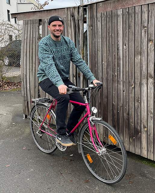 Radverkehrsbeauftragter der Stadt Forchheim Tobias Wilhelm sitzt auf einem pinkfarbenen Herrenrad vor einer hölzernen Bretterwand.