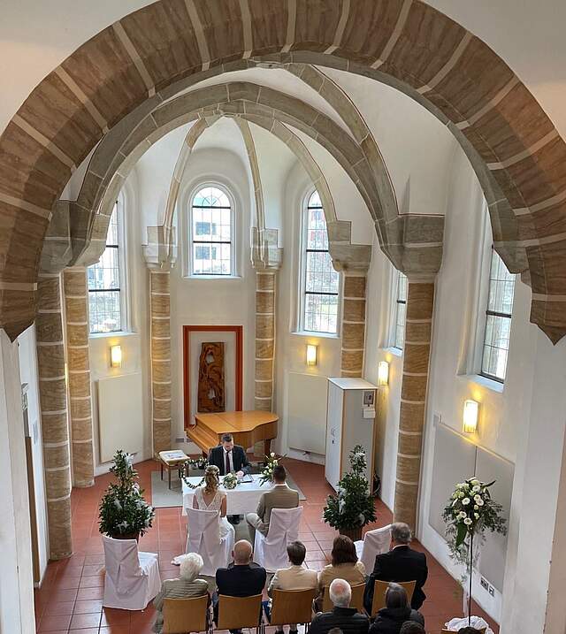 Innenansicht einer Kapelle mit hoher Gewölbedecke, in der eine Trauung stattfindet.