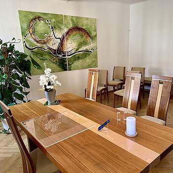 Trauunngszimmer in Forchheim mit stilvollen Holzmöbeln, Zimmerpflanzen, einem großen Wandbild in Grüntönen. Auf dem Tisch des Standesbeamten stehet eine weiße Orchidee, eine weiße Kerze und zwei blaue Füller.