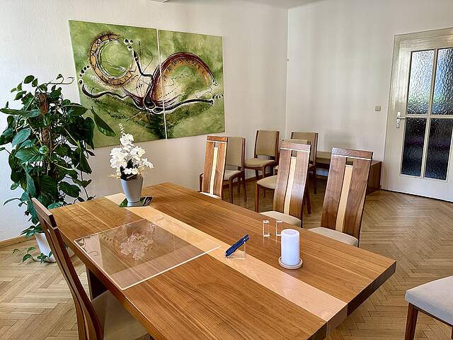 Trauunngszimmer in Forchheim mit stilvollen Holzmöbeln, Zimmerpflanzen, einem großen Wandbild in Grüntönen. Auf dem Tisch des Standesbeamten stehet eine weiße Orchidee, eine weiße Kerze und zwei blaue Füller.