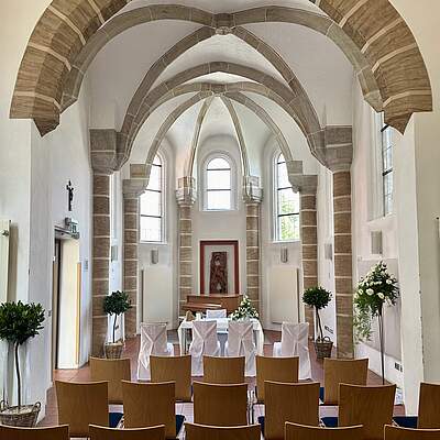 Der Innenraum der Kapelle St. Gereon mit Kreuzbogengewölbe, Stuhlreihen, Blumenschmuck und den weiß geschmückten Tisch des Standesbeamten von der Empore fotografiert.