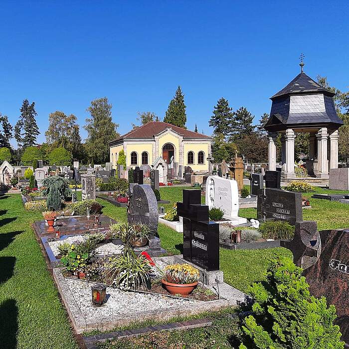 Kolumbarium und Dechant-Reuder-Kapelle im Alten Friedhof im Hintergrund. Im Vordfergrund befinden sich Erdgräber mit Bepflanzung.