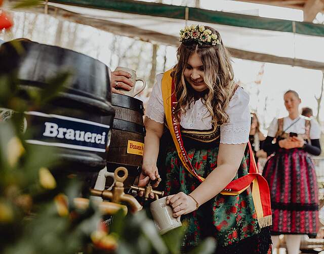 Bierkönigin Luisa I. in Tracht und mit Schärpe Stich ein Fass Bier an.