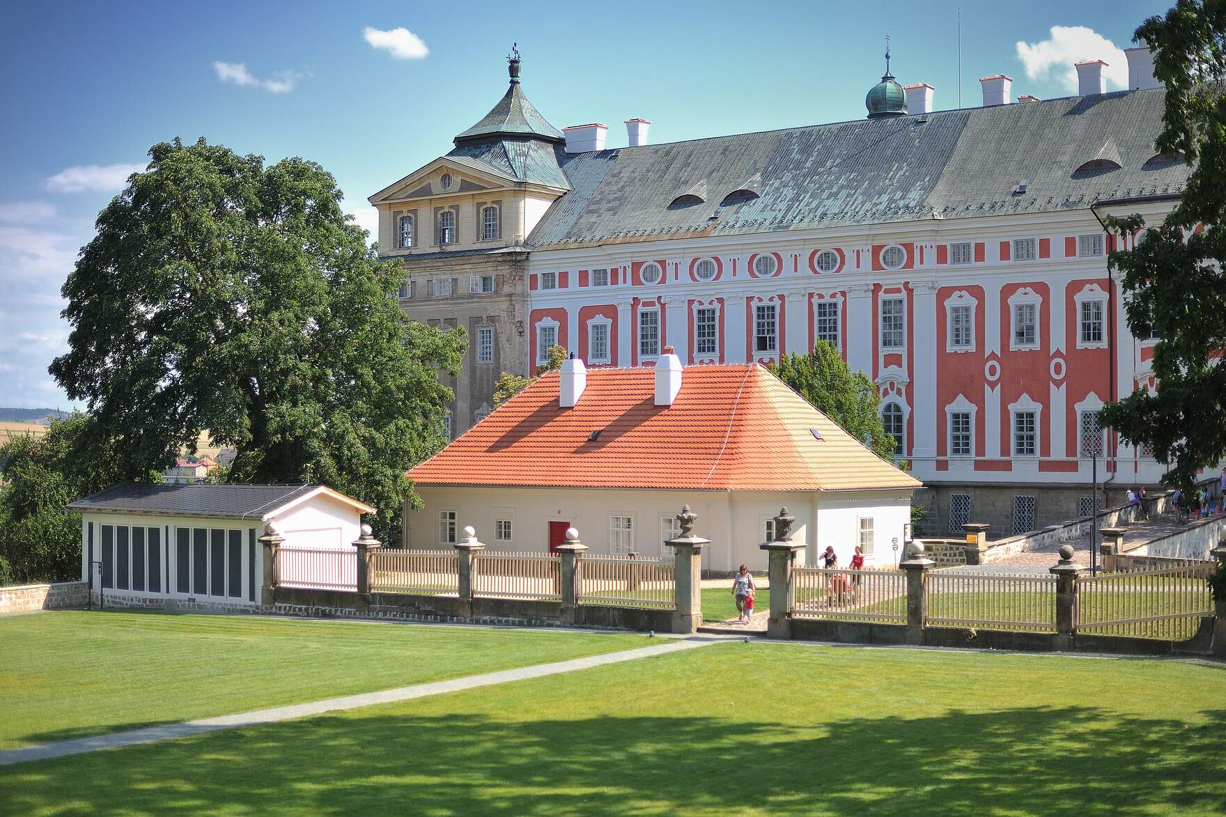 Das barocke Beneditinerkloster in Braunau mit rosa-weißer Fassade in einer großen Parkanlage umgeben von einem Zaun.