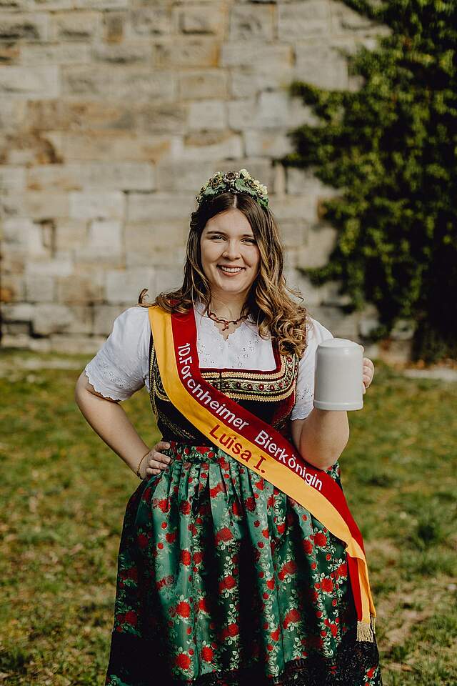 Eine junge Frau trägt eine fränkische bunte Tracht und eine Schärpe. Sie trägt die Krone der Forchheimer Bierkönigin.