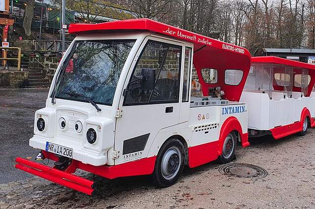 Ein rot-weißer Elektrozug mit einem Personenanhänger.