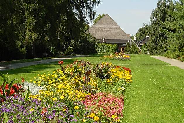 Die Aussegnungshalle am Neuen Freidhof mit Grünfläche und Blumenbeet im Vordergrund