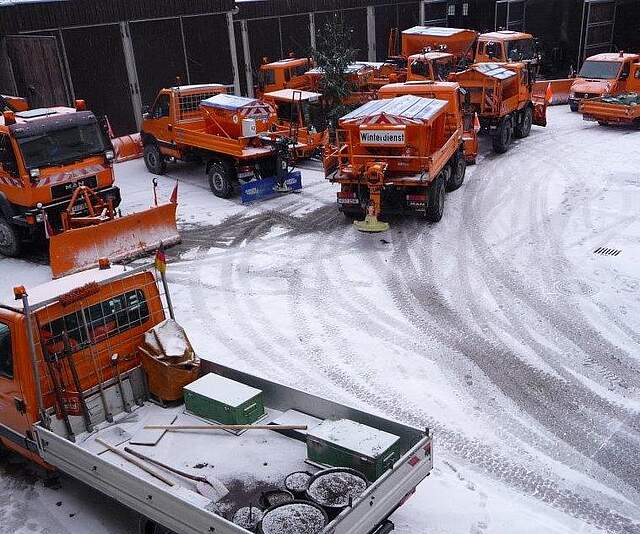 Mehrere Winterräum- und Streufahrzeuge stehen auf einem schneebedeckten Innenhof.