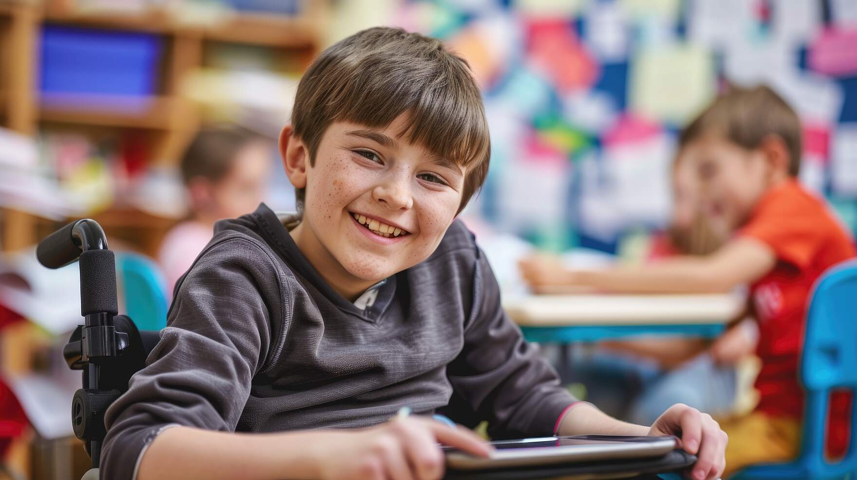 Ein fröhlicher Junge in einem Rollstuhl befindet sich zusammen mit anderen Schülern in einem Klassenraum.