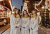 Drei junge Frauen in Engelskostümen auf einem Weihnachtsmarkt.