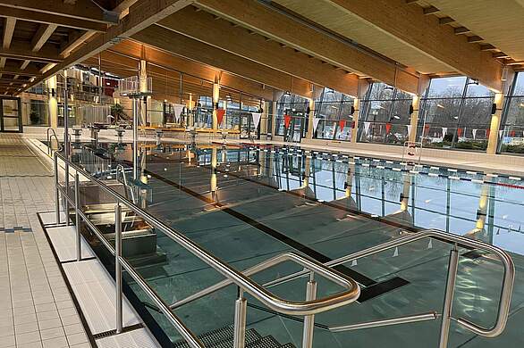 Ein Indoor-Sportschwimmbecken in einem Freizeitbad mit Sprungturm am Ende des Beckens.