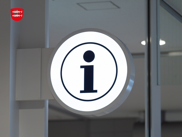 Information der Stadt Forchheim Ein Büro mit Glastrennung und einem beleuchteten runden Schild mit einem Info-Zeichen.