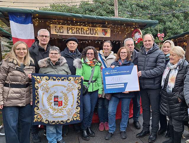 Le Perreux: Besuch aus der Partnerstadt mit Spendenübergabe Eine Gruppe Menschen bei Scheckübergabe vor einer Weihnachtsbude