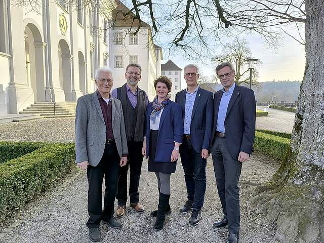 Eine Gruppe aus vier Männern und einer Frau in der Mitte steht in einem Park vor dem Kloster St. Urban.