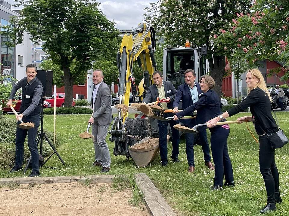 Der offizielle Spatenstich am Streckerplatz (v.l.): René Franz, Leiter des Stadtbauamtes, Bürgermeister Udo Schönfelder, Andreas Geck, Leiter des Amtes für Öffentliches Grün und Biodiversität, Bernd Endres, Leiter des Bereichs Planung und Bau der Regierung von Oberfranken, Bürgermeisterin Dr. Annette Prechtel und die Leiterin des Amtes für Stadt- und Verkehrsplanung/ Umwelt- und Naturschutz, Corinna Stirnweiß. Im Hintergrund befinden sich große Bäume und ein Ausschnitt des Gebäudes des Landratsamtes Forchheim