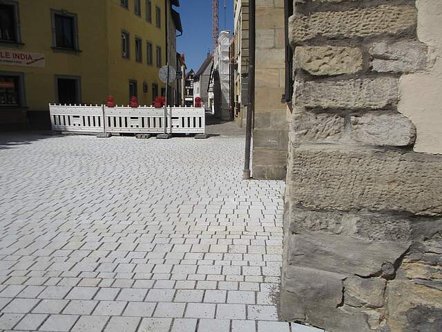 Neue grau gepflasterte Straßenfläche in einer Stadt. Im Hintergrund befindet sich eine Straßensperre.