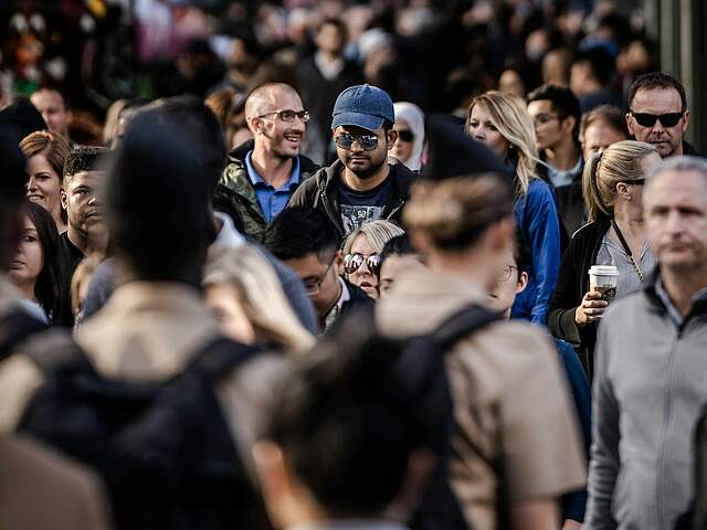 Personen in einer Menschenmenge sind in der Mitte fokussiert, im Vorder- und Hintergrund verschwommen zu sehen.