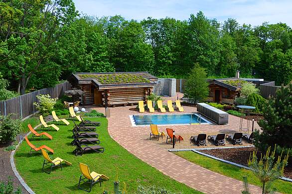 Saunaaußenbereich mit Liegeflächen und Liegewiesen sowie einem kleinen Schwimmbecken und einer Blocksauna im Hintergrund.