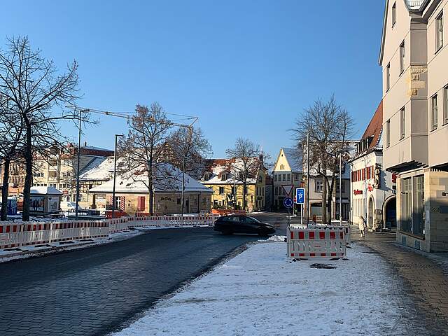 Die Pflasterarbeiten an einem Kreisverkehr in einer Stadt sind abgeschlossen. Dahinter befinden sich noch Absperrgitter zu einer Baustelle.