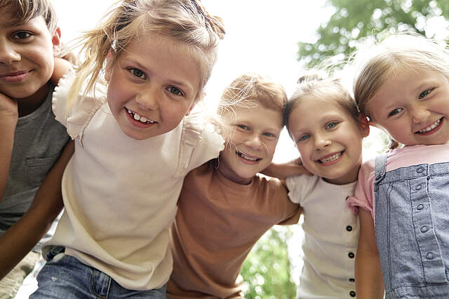 Lachende Kinder beim Sommerferienprogramm Nahaufnahme des Portraits von Kindern, die sich zusammen umarmen.