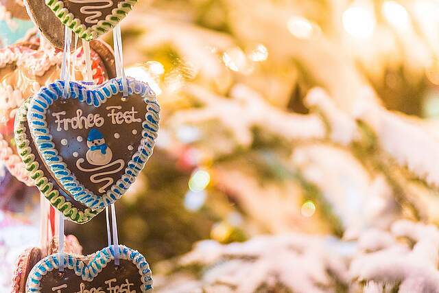 aufgefädelte Lebkuchenherzen an einem weihnachtlich geschmücktem Stand mit der Aufschrift "Frohes Fest".