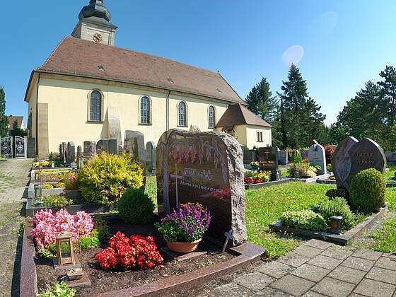 Gräber auf einem Friedhof. Im Hintergrund befindet sich eine Kirche