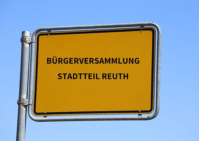 Ortsstschild vor blauem Himmel mit der Aufschrift "Bürgerversammlung Stadtteil Reuth".