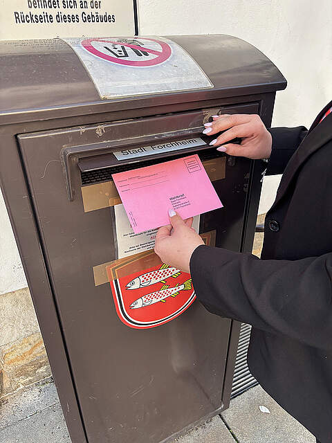 Briefwahl Eine Person wirft einen Wahlbrief in einen Briefkasten.