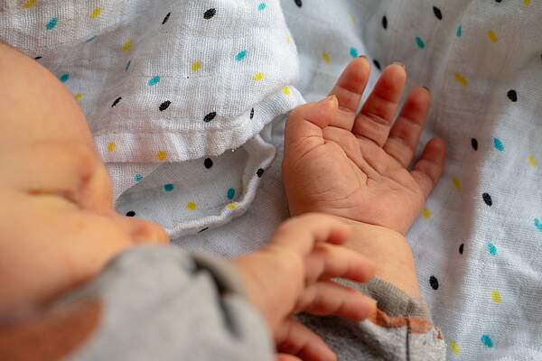 Ausschnitt eines Gesichts und die Arme eines neugeborenes Babys, das auf einer Babydecke liegt.