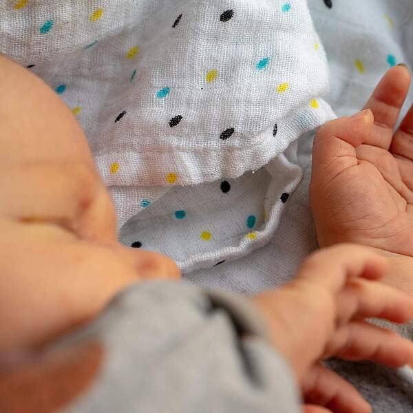 Ausschnitt eines Gesichts und die Arme eines neugeborenes Babys, das auf einer Babydecke liegt.