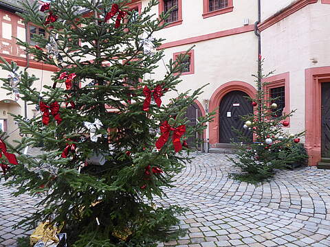 Innenhof eines historischen Schlosses mit weihnachtlich geschmückten Christbäumen.