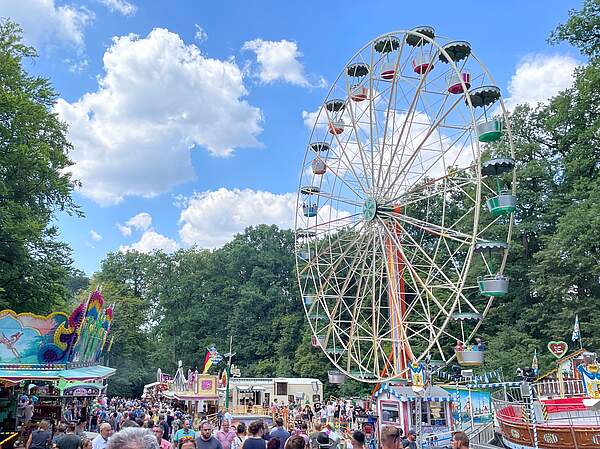 Der gut besuchte Festplatz des Annafestes mit Fahrgeschäften und Riesenrad bei sonnigen Wetter.