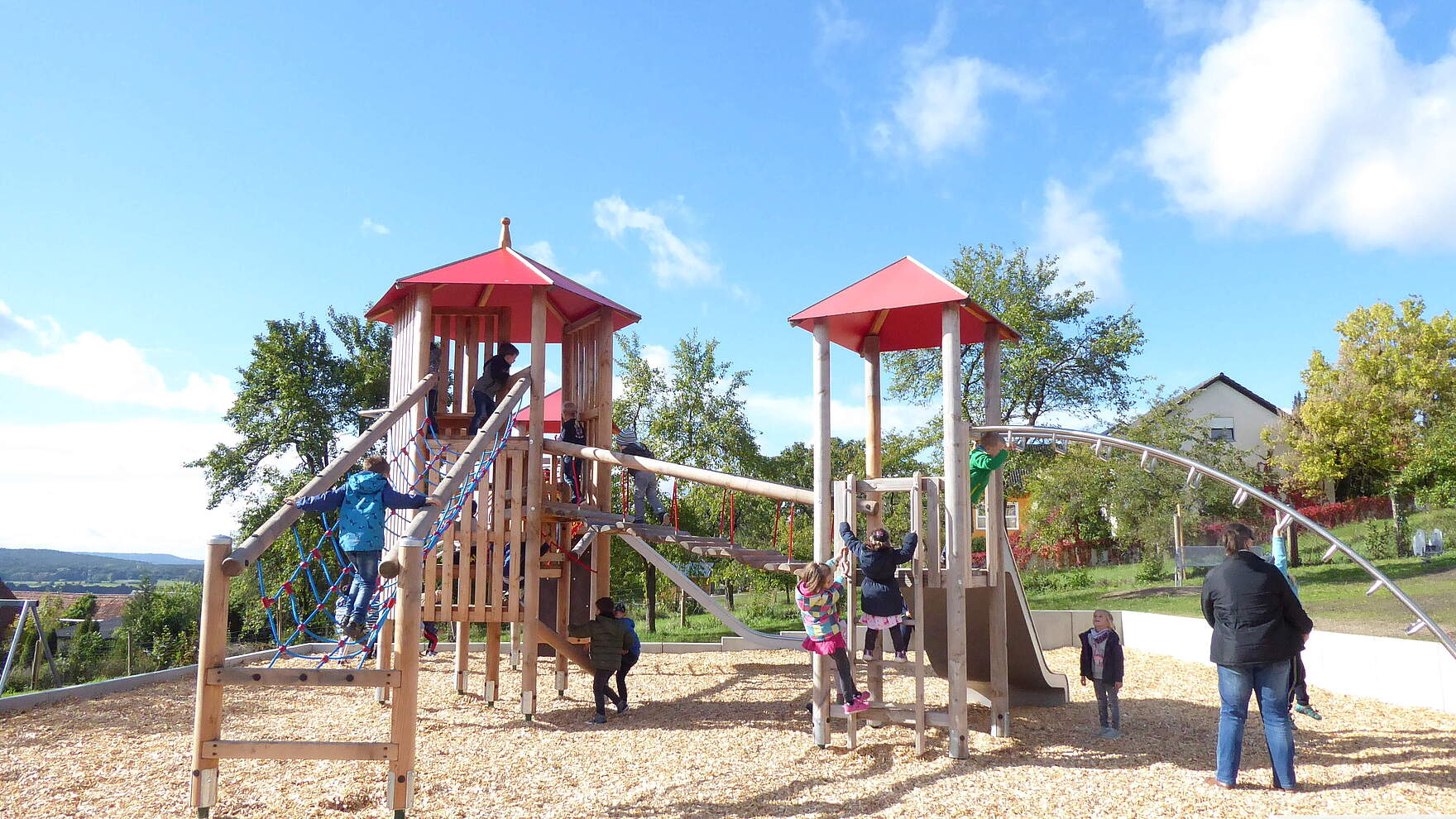 Kinder spielen auf zwei miteinander verbunden Spieltürme mit Balancier- und Klettermöglichkeiten auf einem neu angelegten Spielplatz.