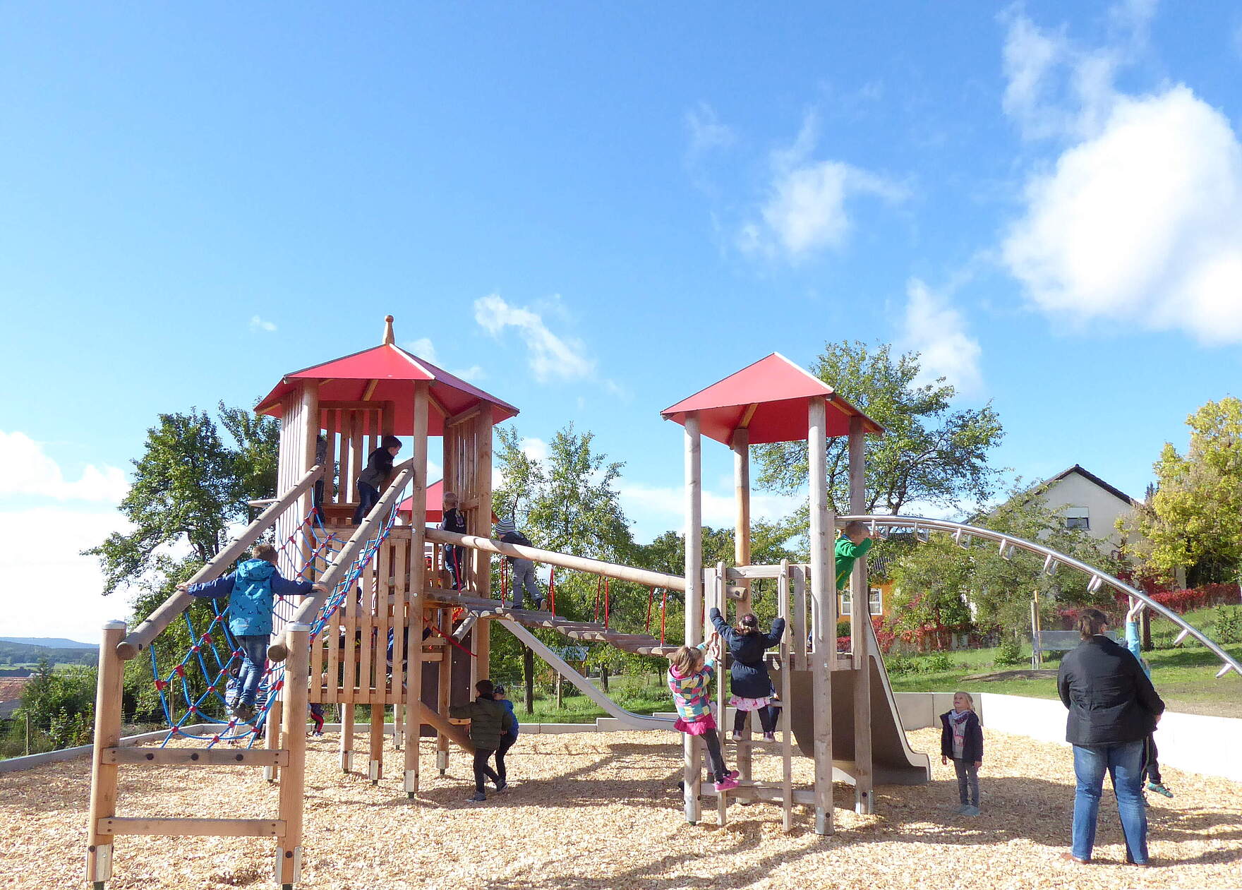 Kinder spielen auf zwei miteinander verbunden Spieltürme mit Balancier- und Klettermöglichkeiten auf einem neu angelegten Spielplatz.