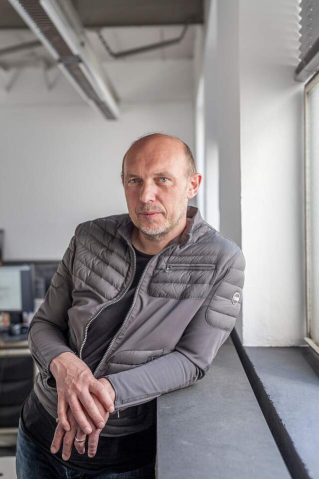 Ein Mann lehnt in einem Büro an einer Fensterbank.