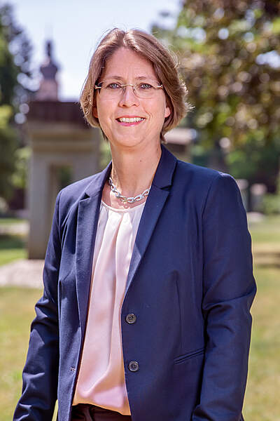 Bürgermeisterin Dr. Annette Prechtel steht bei Sonnenschein im Stadtpark. Im Hintergrund sieht man die Kirchturmspitze der Martinskirche.