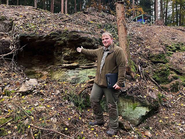 Ein Förster zeigt auf eine kleine Felsenhöhle 