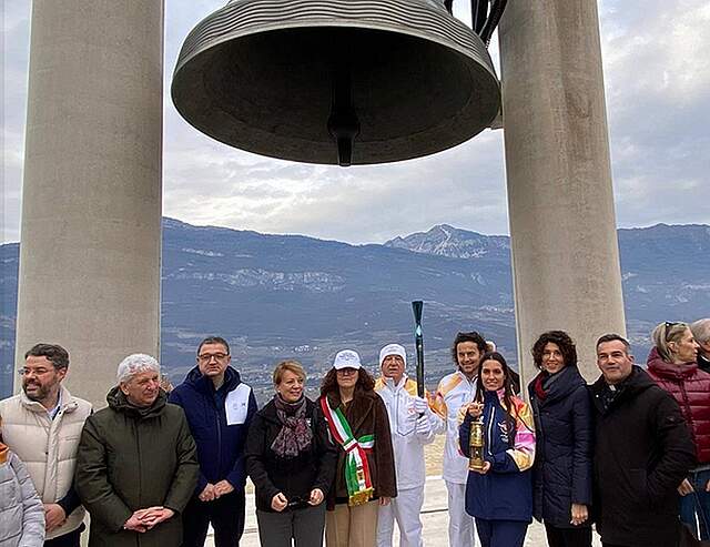 Olympisches Feuer in Rovereto - Zwischenstopp an der Friedenglocke Mehrere Personen stehen vor der Friedensglocke in Rovereto